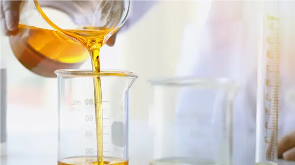 Image of amber viscous oil being poured into a glass beaker for testing.